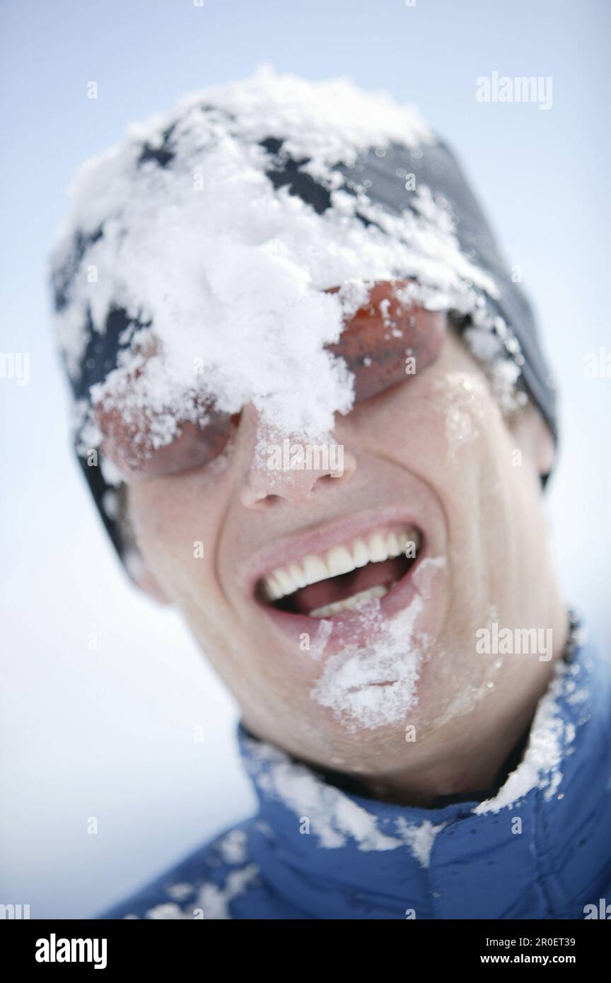 Junger Mann mit Schnee im Gesicht, lachend Stockfoto