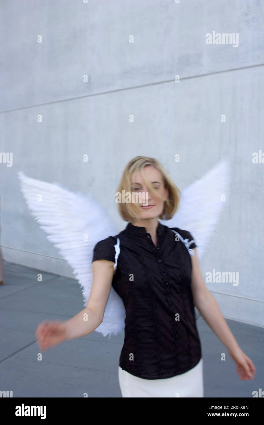 Mittelgroße Erwachsene Frau mit Engelsflügeln in der Nähe einer Betonwand Stockfoto