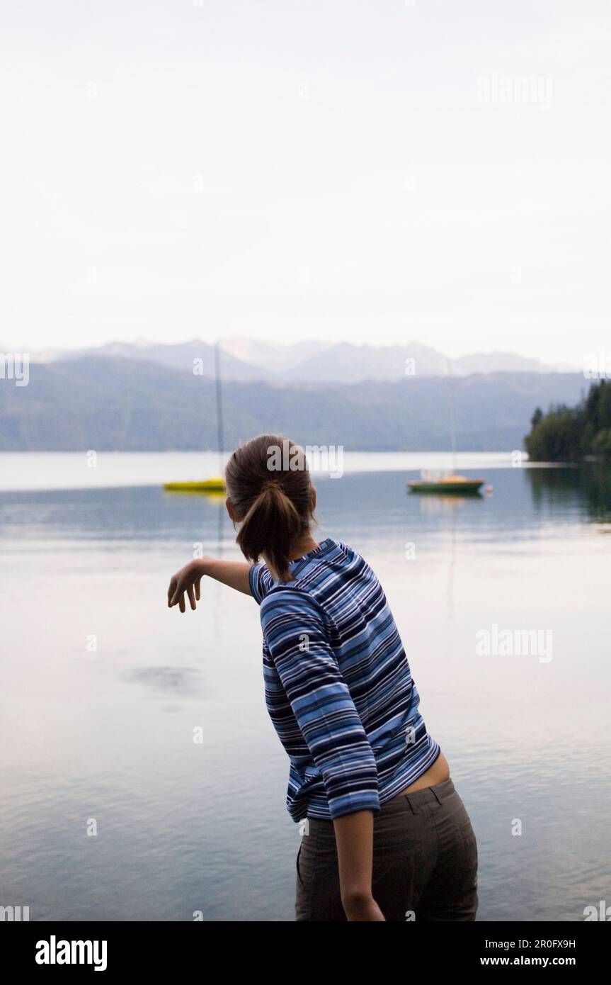 Eine junge Frau wirft einen Stein in den Walchensee, Bayern, Deutschland Stockfoto