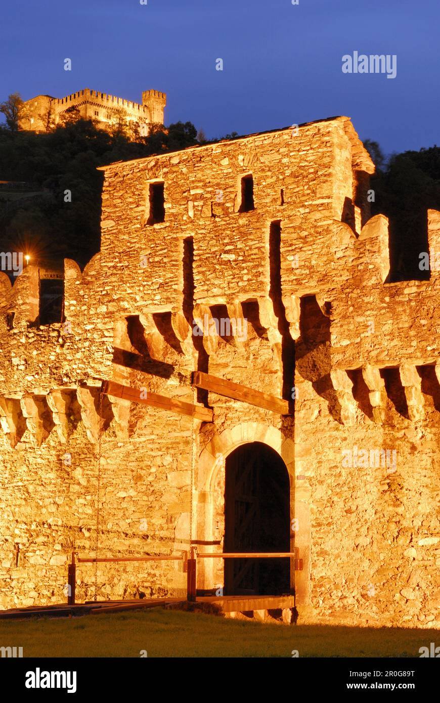 Beleuchtete Zugbrücke von Schloss Castello di Montebello mit Schloss Castello di Sasso Corbaro im Hintergrund in der UNESCO-Weltkulturerbestätte Bellinzona, Stockfoto