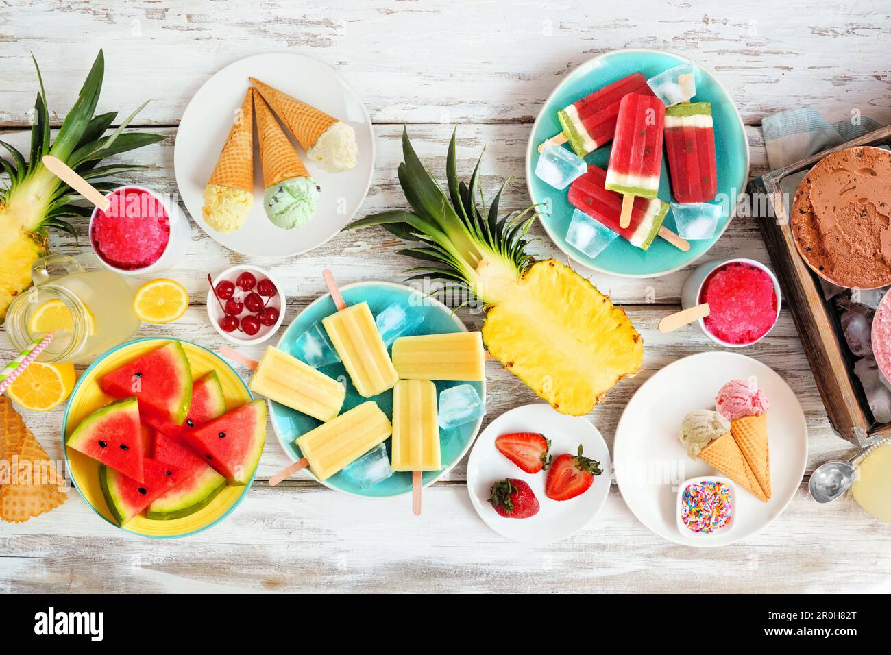 Tischszene mit coolen Sommergerichten. Sammlung von Eis, Eis am Stiel und Obst. Blick von oben auf rustikalen weißen Holzhintergrund. Stockfoto