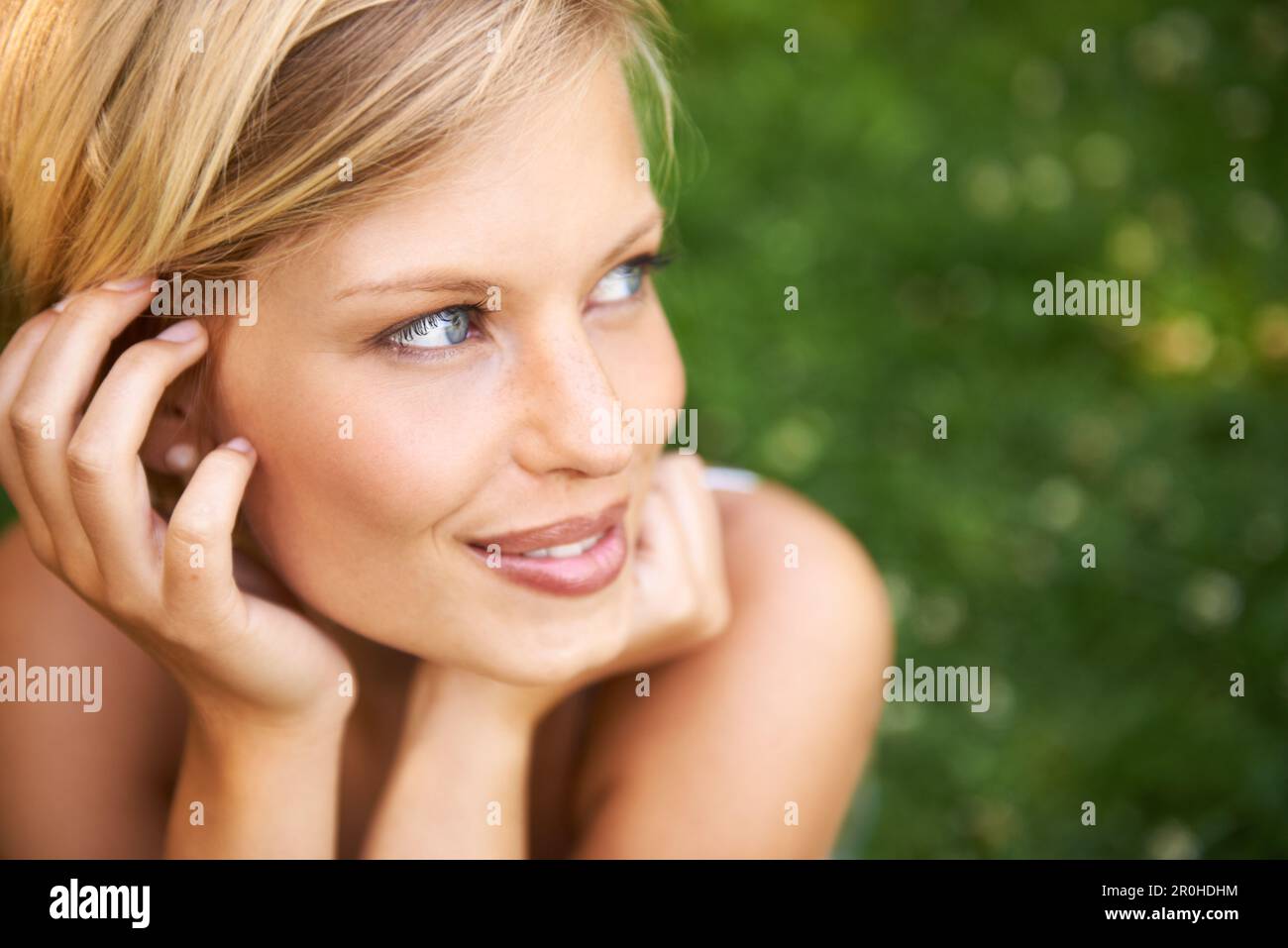 Sommertagsträume mit einem Lächeln. Attraktive junge blonde Frau, die draußen auf dem Gras sitzt und lächelt. Stockfoto