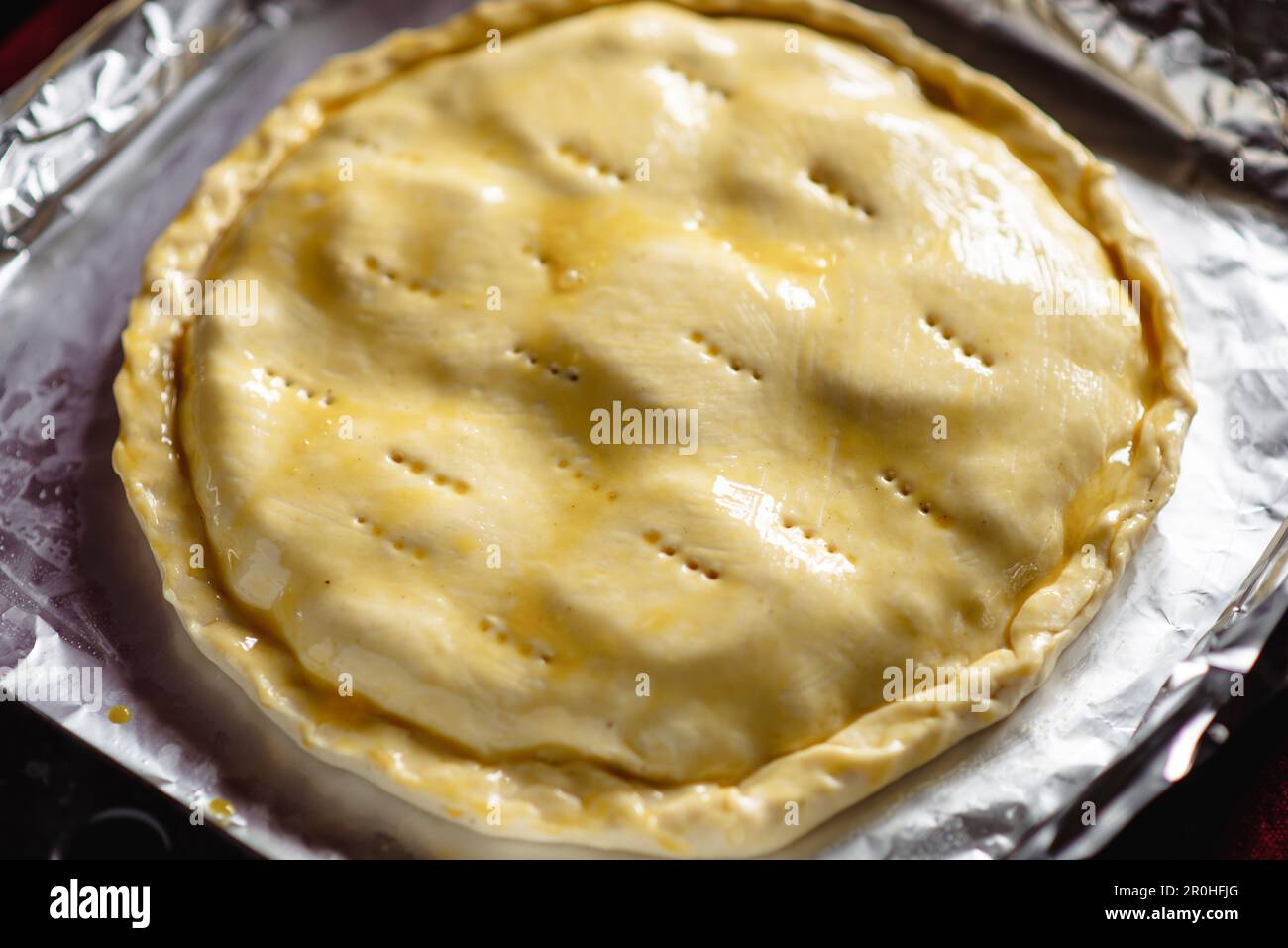 Ich mache einen geschlossenen Kuchen. Runde rohe Torte auf einem Backblech. Mit Hühnchen-Eigelb auftragen. Stockfoto