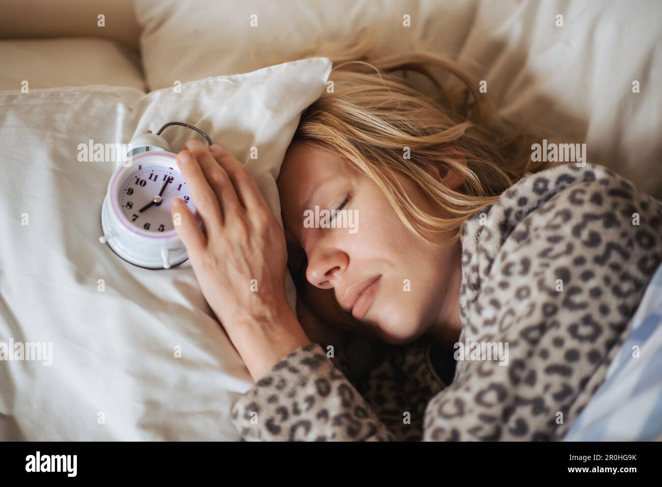 Wecker und schlafende Frau. Der Begriff Schlafprobleme, Schlaflosigkeit, zirkadianer Rhythmus. Stockfoto