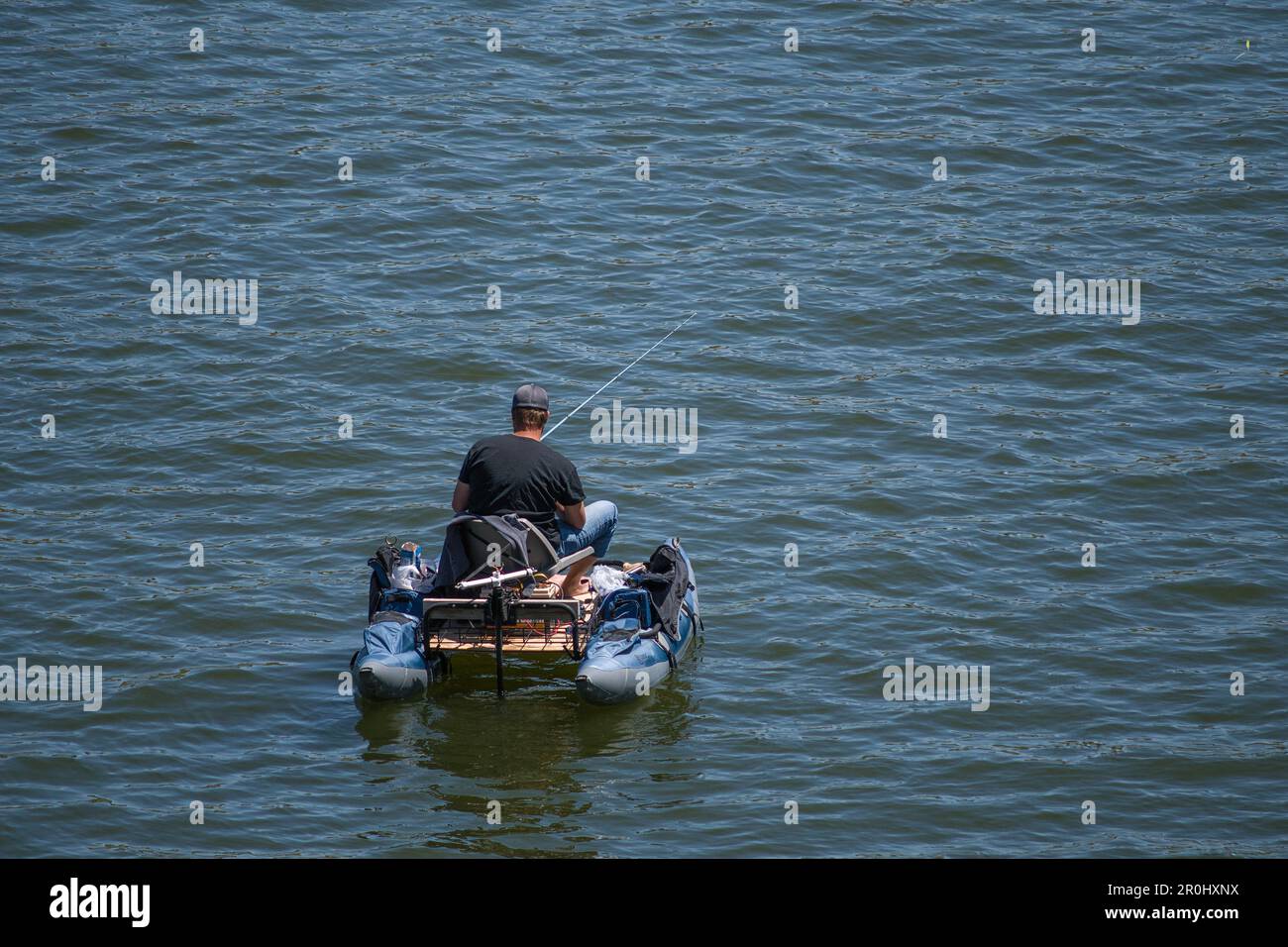 Ein Mann in einem schwarzen Hemd, der auf einem nautischen Schiff auf einem See angeln und es an diesem sonnigen Tag als Transportmittel benutzt Stockfoto