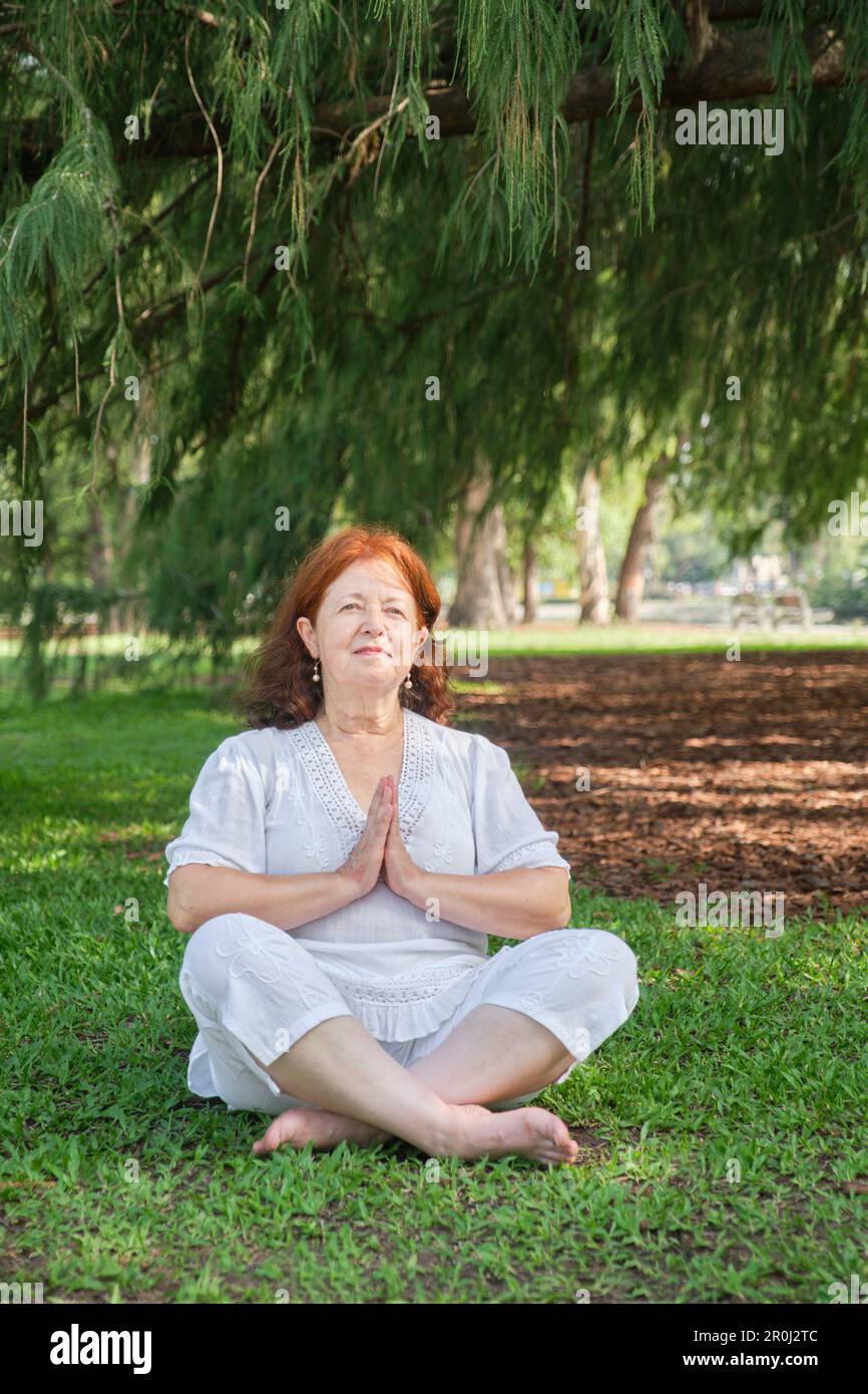 Porträt einer erwachsenen lateinerin in weißer Kleidung, die lächelt, während sie im Park Yoga im Freien praktiziert. Konzepte: Wellness, Ruhe und psychische Gesundheit. Stockfoto