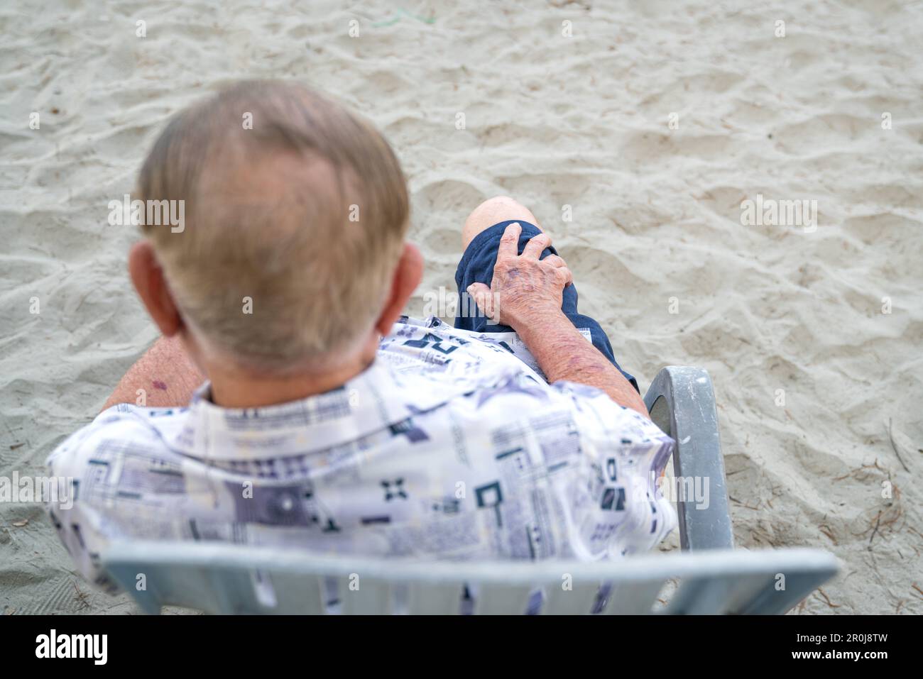 Blick von hinten und oben auf einen älteren Asiaten, der auf einem Stuhl sitzt. Selektive Fokussierung auf seine Hand. Alterungskonzept. Stockfoto