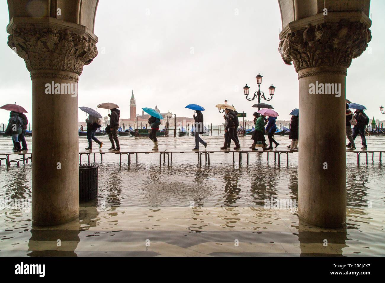Touristen mit Sonnenschirmen und Plastikschuhen, Gummistiefeln, gehen auf Passarellenwegen während der Acqua alta in der Nähe des Dogenpalastes, des Markusplatzes, S. Stockfoto