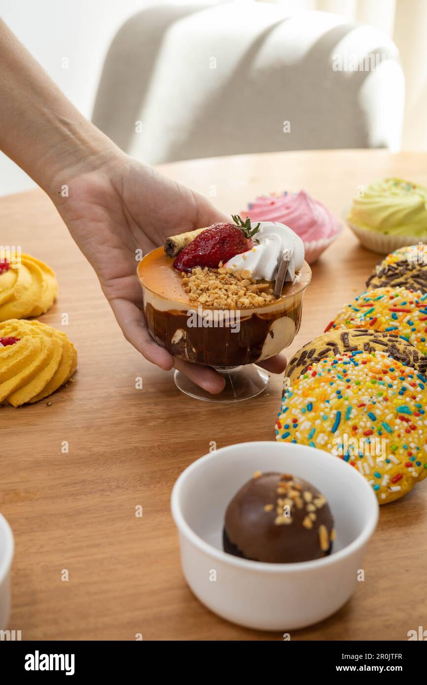 Serviertisch mit exquisiten Desserts, dazu Tasse mit Eiscreme, Sahne und Erdbeere, kongeösen Plätzchen und Schokoladenball, appetitlich Stockfoto