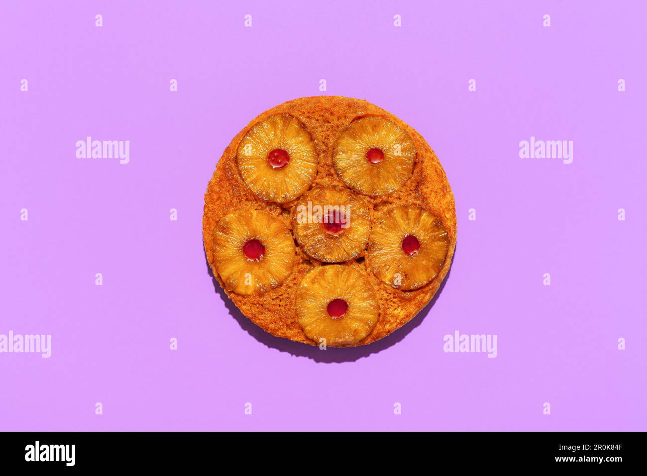 Blick von oben mit hausgemachtem Ananaskuchen, minimalistisch auf einem lilafarbenen Tisch. Upside-down-Kuchen mit Ananas- und Erdbeermarmelade. Stockfoto
