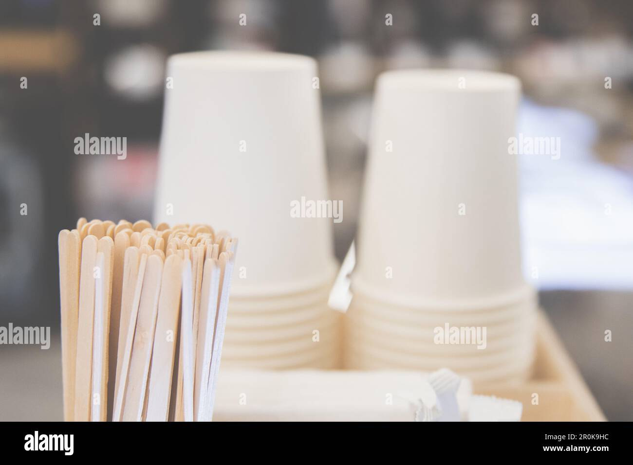 Hintergrund mit Pappbechern und Rührstäbchen neben einer Kaffeemaschine, gemütliche Atmosphäre eines Cafés Stockfoto