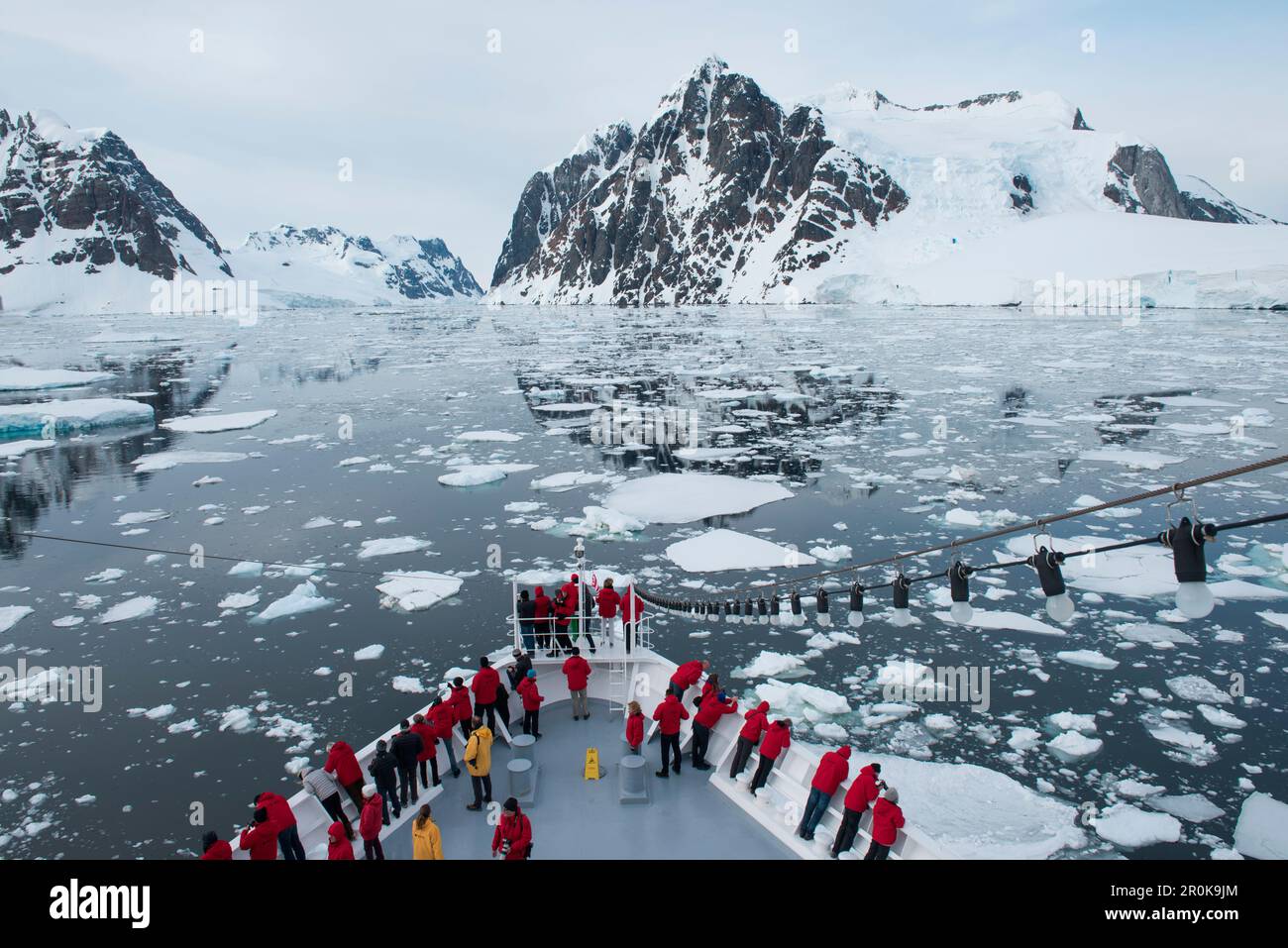 Menschen am Bug des Expeditionsschiffes MS Bremen (Hapag-Lloyd Cruises) mit Eisschollen und schneebedeckten Bergen dahinter Stockfoto