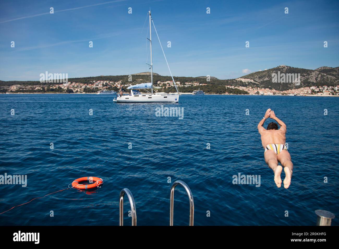 Der Mann springt von der Schwimmplattform des Kreuzfahrtschiffs MS Romantic Star (Reisebüro Mittelthurgau) in die Adria mit dem Segelboot dahinter, in der Nähe von Hvar, Split-Da Stockfoto