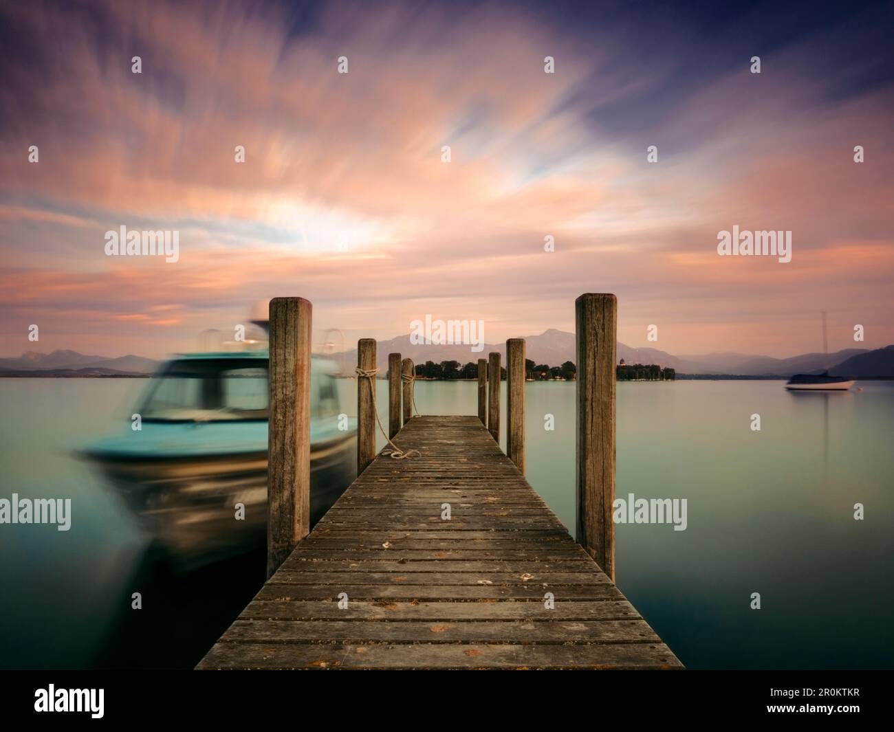 Blick über eine Fußgängerbrücke zur Fraueninsel und den Chiemgau-Alpen an einem Sommerabend, Gstadt am Chiemsee, Oberbayern, Deutschland Stockfoto