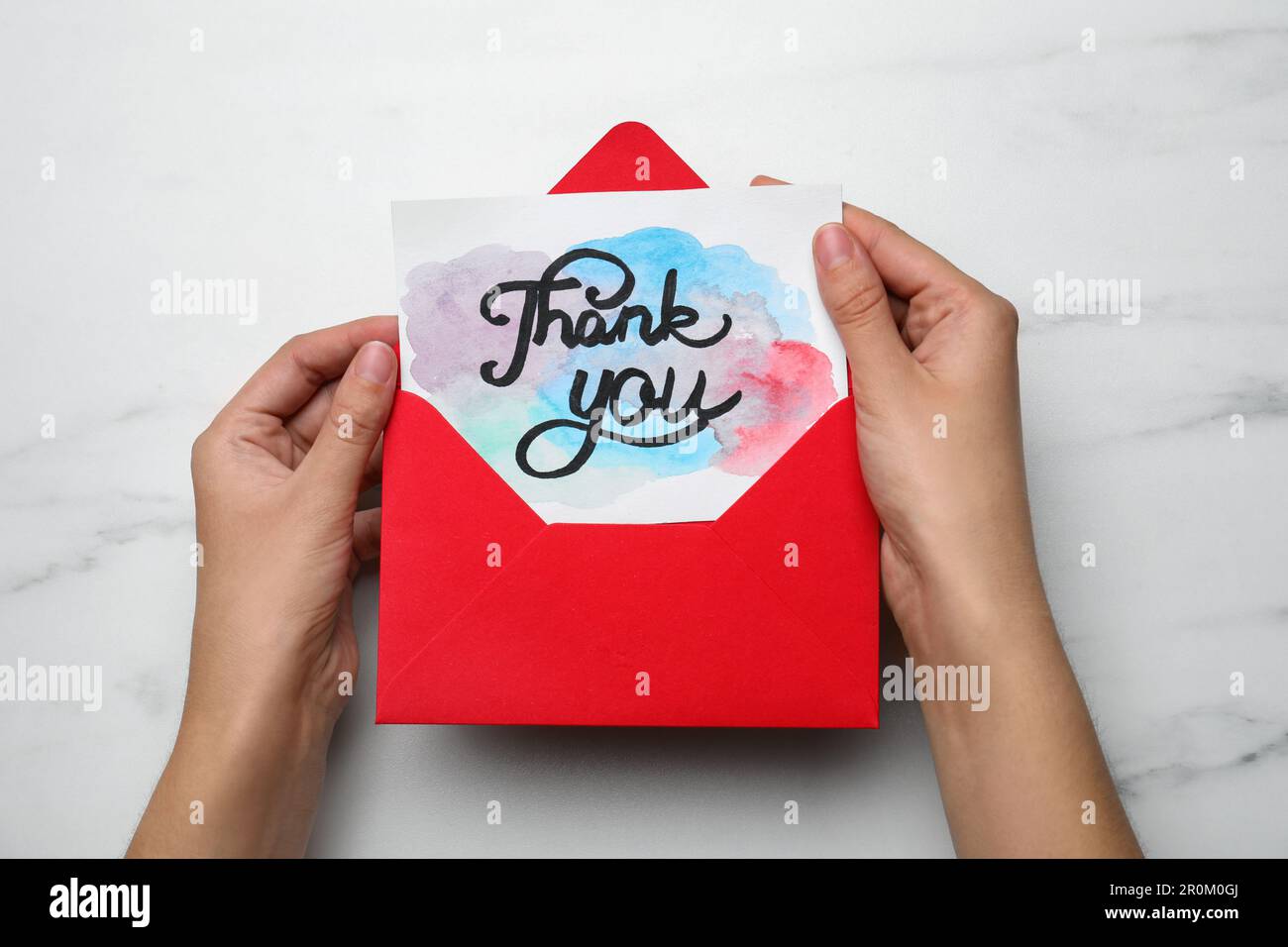 Frau mit Umschlag und Karte mit Phrase Danke am weißen Marmortisch, Draufsicht Stockfoto