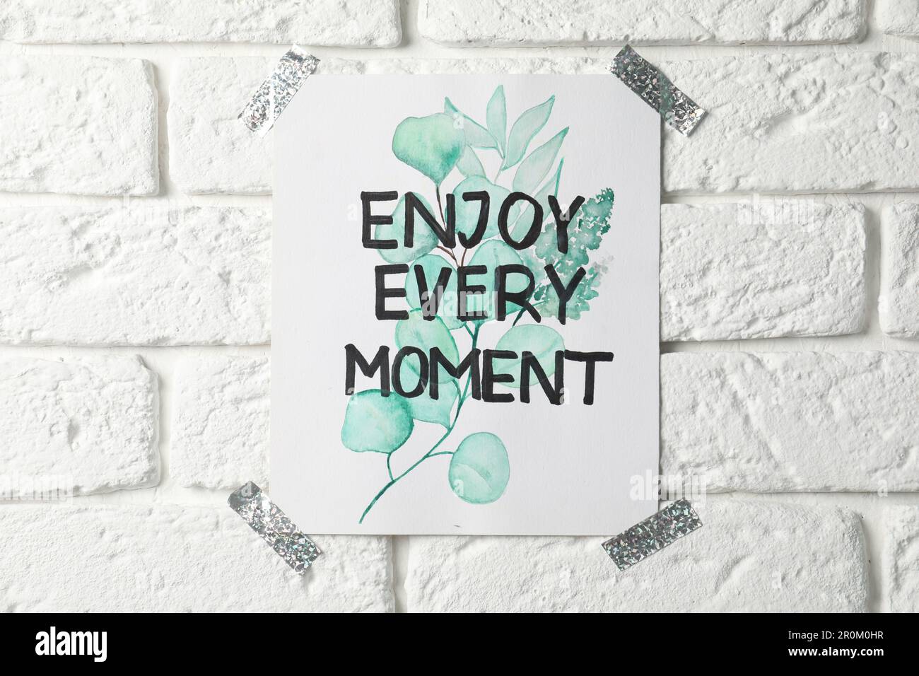 Karte mit Text Genießen Sie jeden Moment an der weißen Backsteinwand Stockfoto