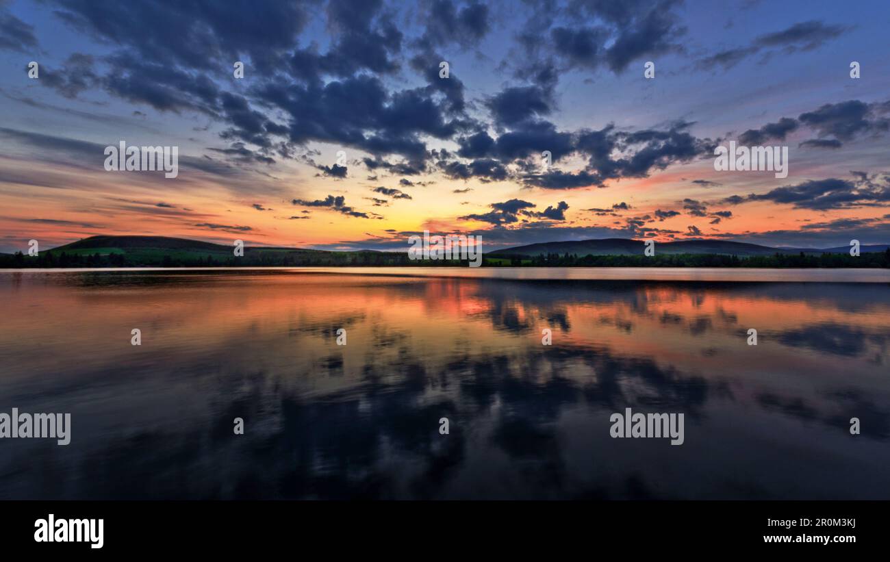 Eine atemberaubende spiegelartige Reflexion eines Sonnenuntergangs über dem Wasser am malerischen Loch von Lintrathen, Angus, Schottland. Stockfoto
