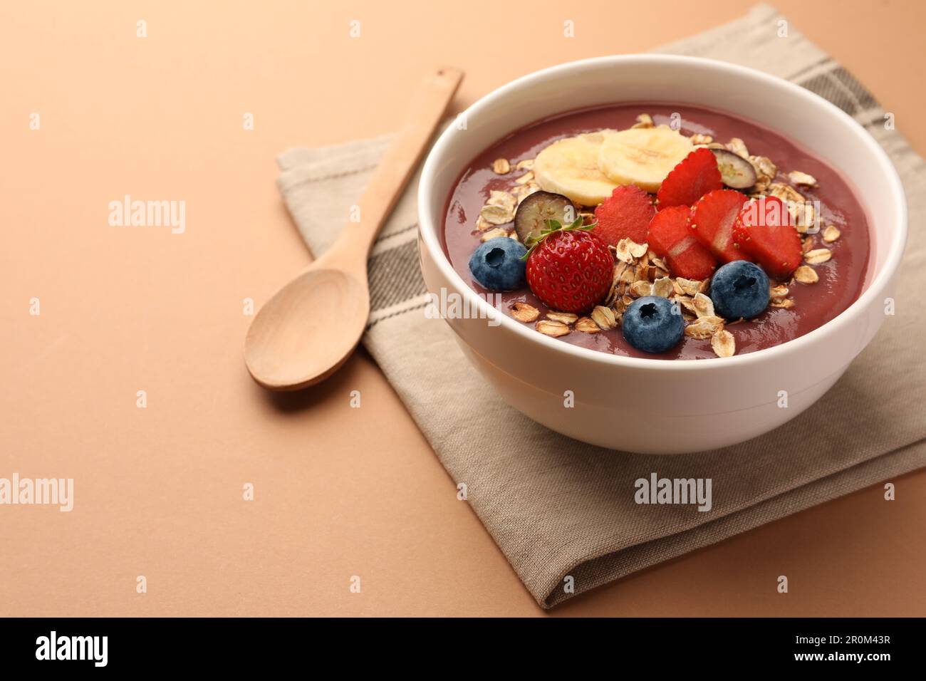Köstliche Smoothie-Schüssel mit frischen Beeren, Banane und Müsli auf blassorangefarbenem Hintergrund. Platz für Text Stockfoto