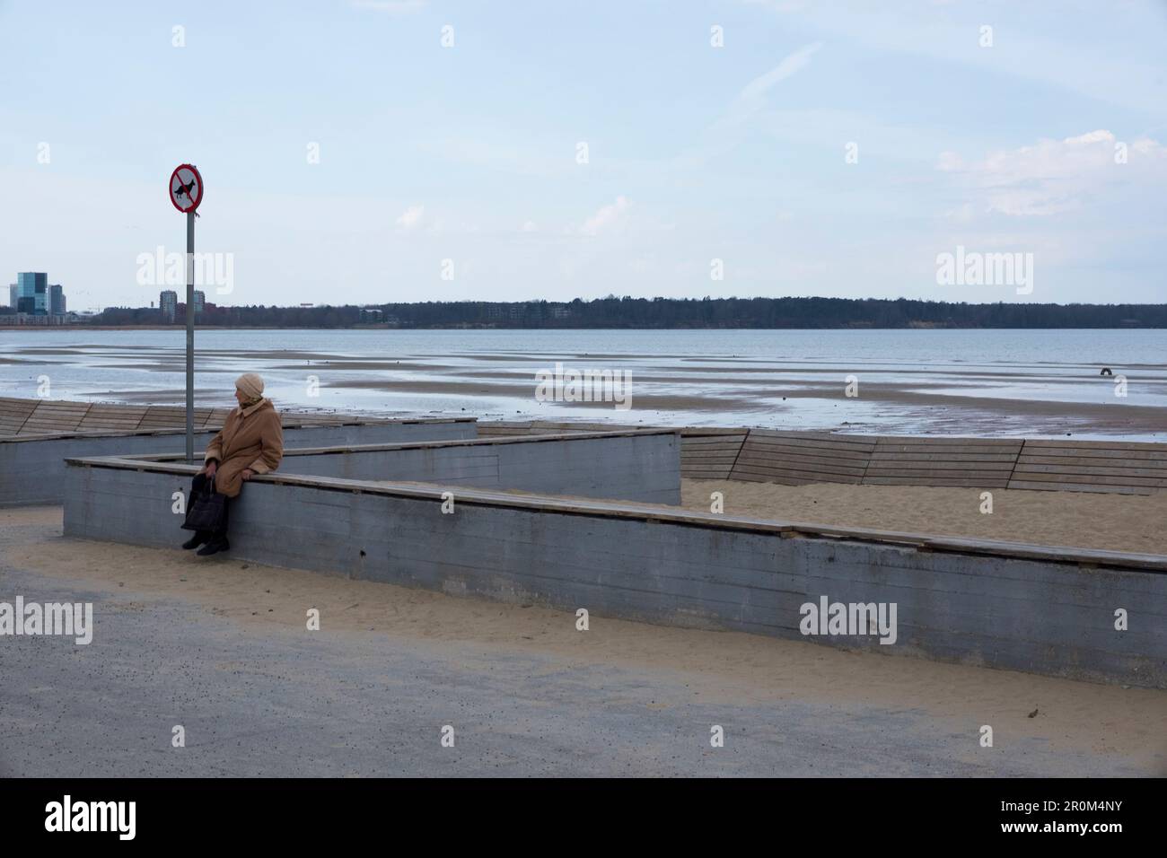 Ältere Frau, die an der Wand am Rande von Stroomi Beach sitzt, Tallinn, Estland. Stockfoto