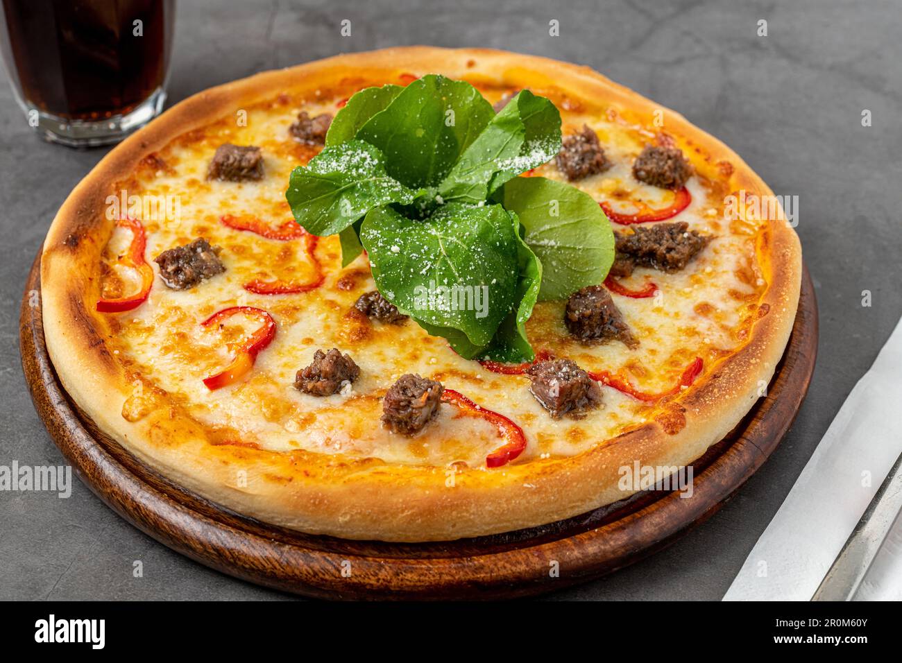 Pizza mit Paprika und Roastbeef auf dem Schneidebrett auf einem Steintisch Stockfoto