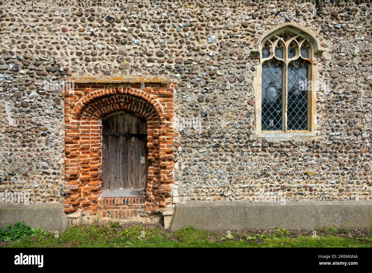 Südtür aus rotem Backstein und Steinfenster in einer mit Stolz verkleideten Steinmauer an der Kirche St. Peter in Weston, Suffolk Stockfoto