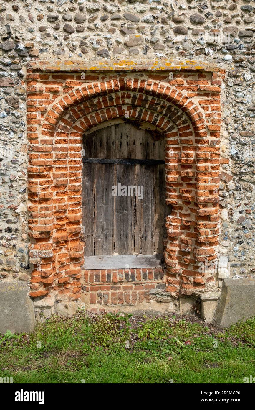 Südtür aus rotem Backstein in einer mit Stolz verkleideten Steinmauer an der Kirche St. Peter in Weston, Suffolk Stockfoto