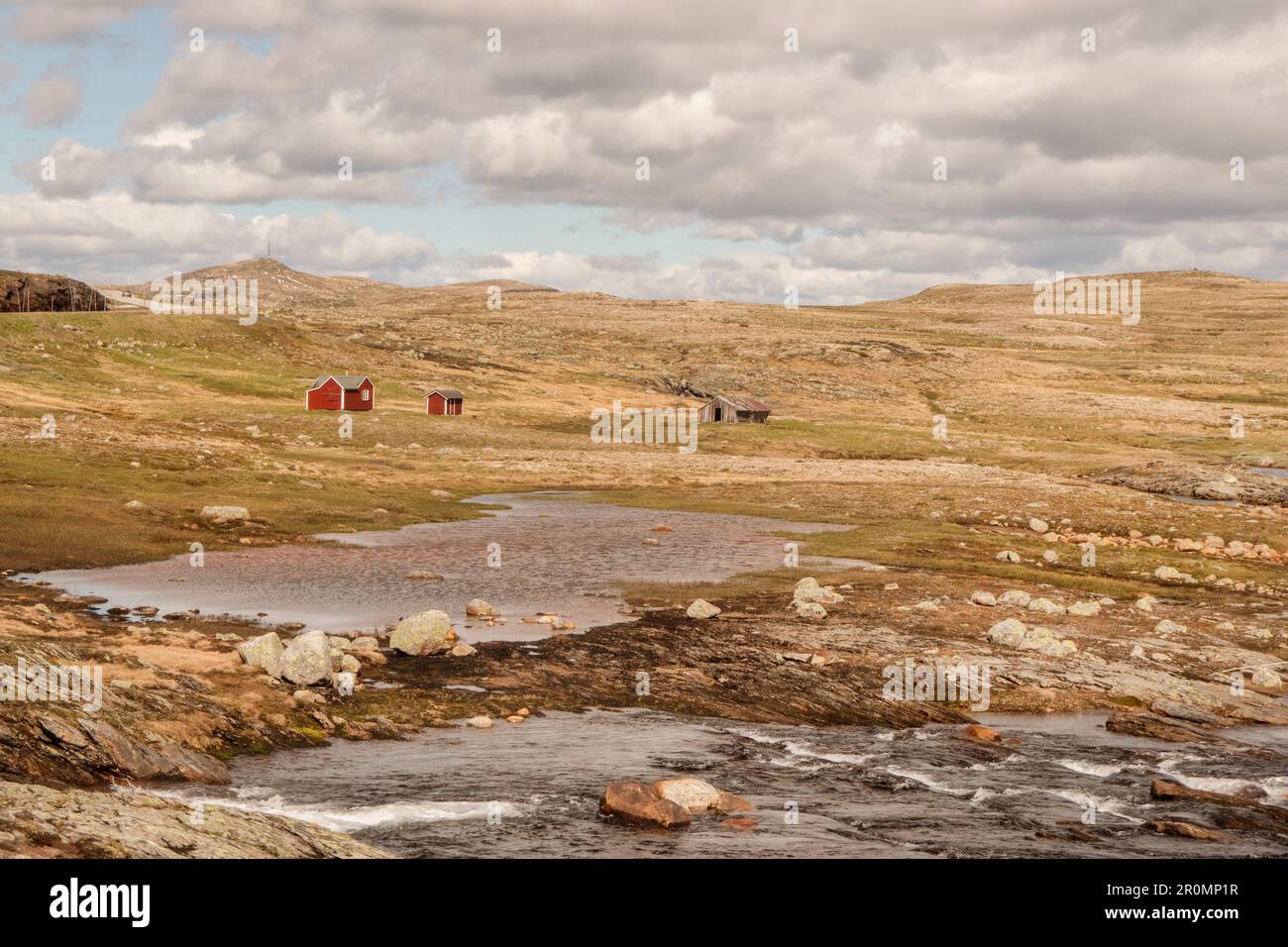 2 rote norwegische Hütten stehen in den Bergen Norwegens. In Finse. Umgeben von einer kargen Landschaft mit Wiesen, Wasser und Steinen Stockfoto