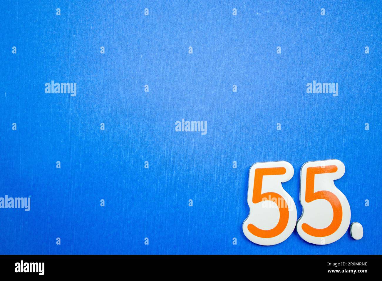 Die Zahl 55, orange und hellblau, von oben fotografiert, auf dem Rand eines blauen Hintergrunds platziert. Stockfoto