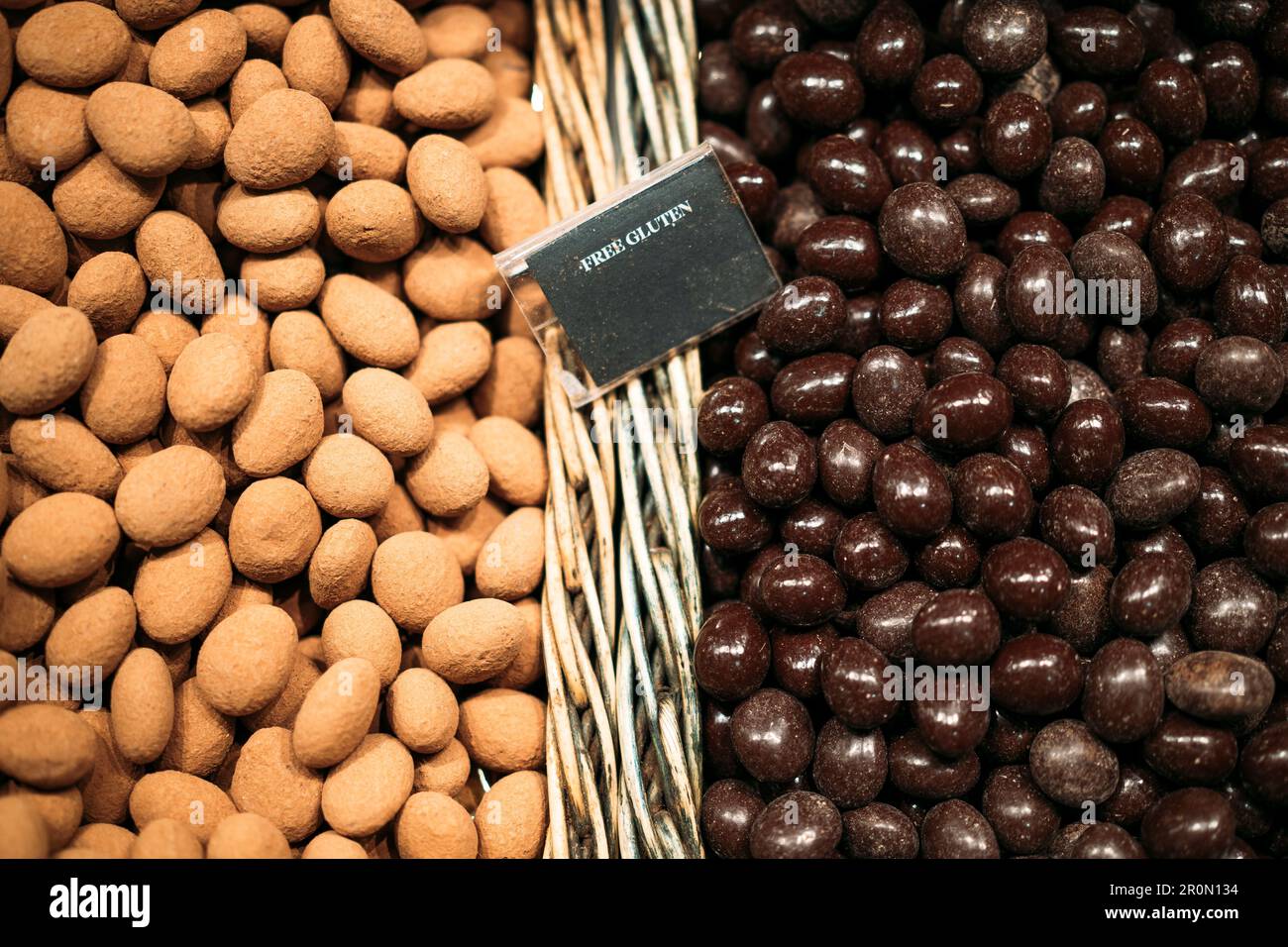 Draufsicht auf verschiedene Haufen glasierter Erdnüsse in Korbkörben mit glutenfreier Inschrift auf dem lokalen Markt in Barcelona Stockfoto