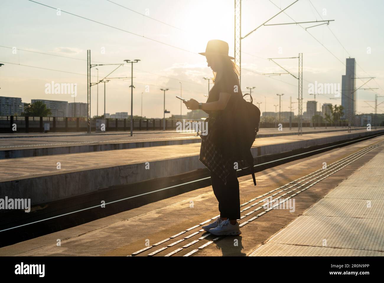 Eine Touristin mit Rucksack, die auf dem Bahnhofsstand stand stand und bei Sonnenuntergang telefonierte. Stockfoto