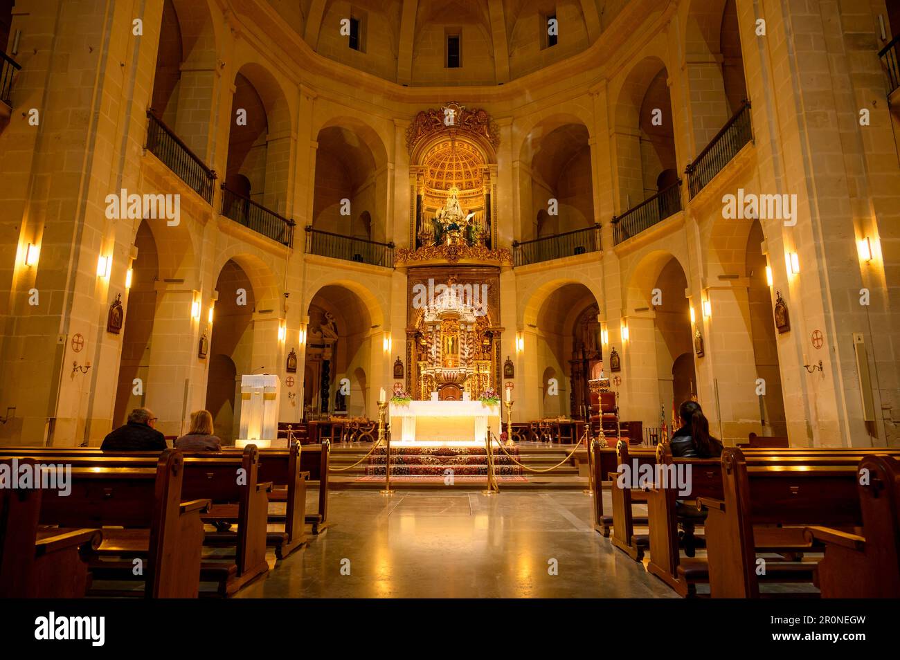 Menschen, die nachts in der Kathedrale von St. Nicolas de Bari beten. Symmetrie von Altar, Säulen und Bänken. Der Altar an der Front. Stockfoto