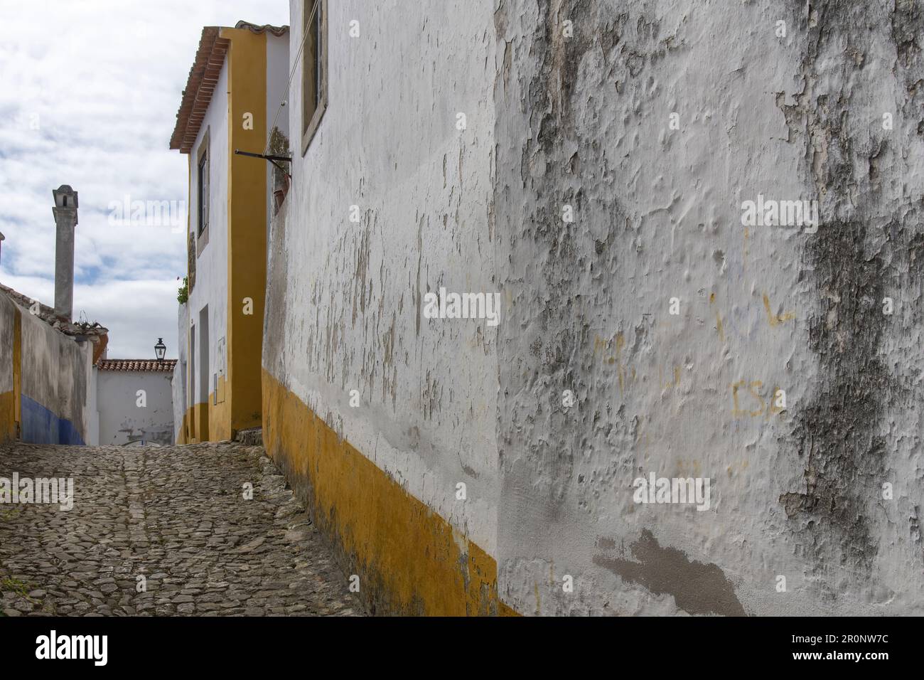 Niedriger Winkel Blick auf eine der kopfsteingepflasterten Straßen von Obidos, Portugal mit typischer mittelalterlicher Architektur mit weiß verputzten Gebäuden und blauem und Stockfoto