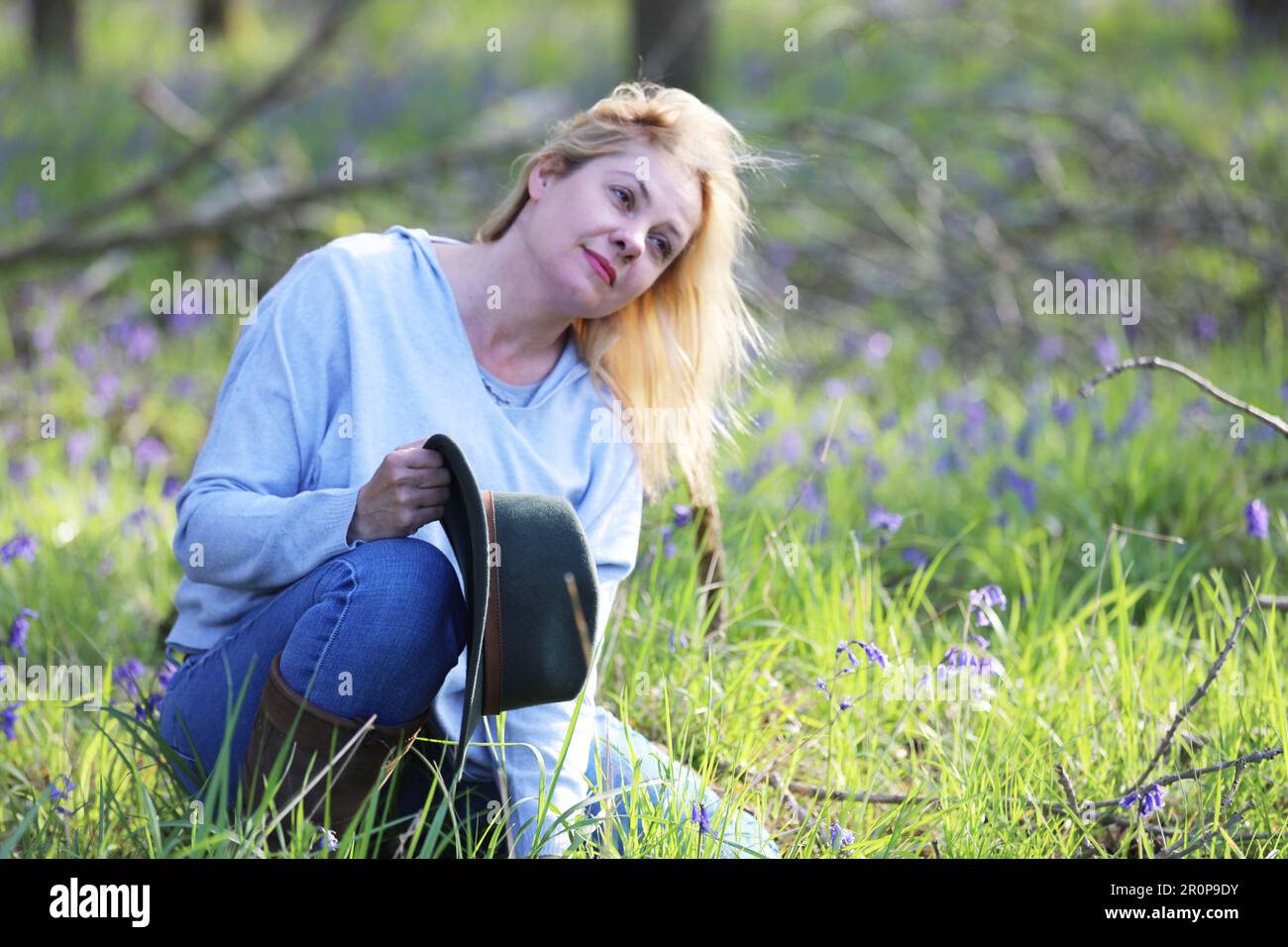 Eine Frau, die in einem Bluebell-Holz sitzt und einen Hut hält Stockfoto