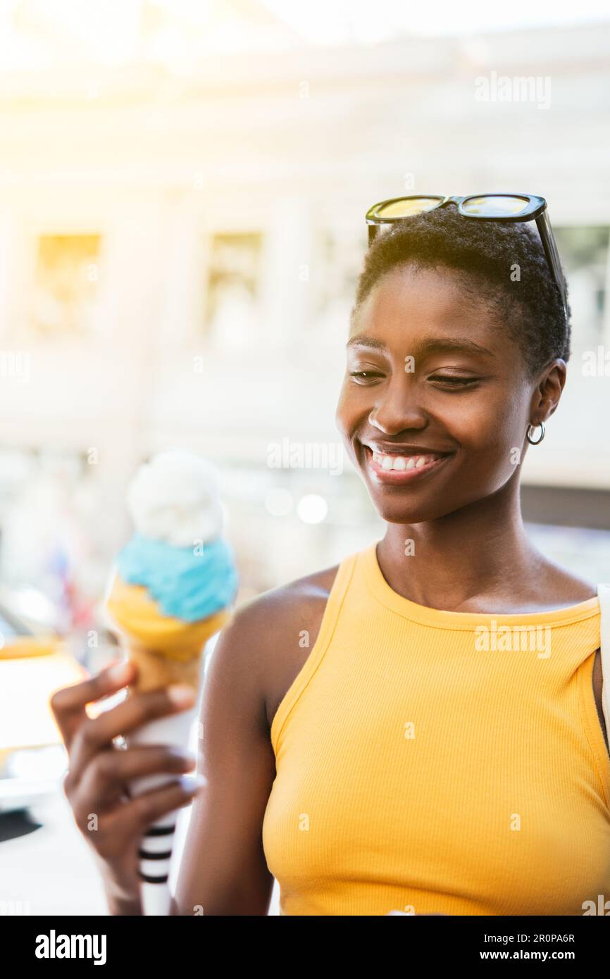 afrikanische Frau, die ein Eis isst. Sie ist an einem sonnigen Sommertag auf der Straße Stockfoto