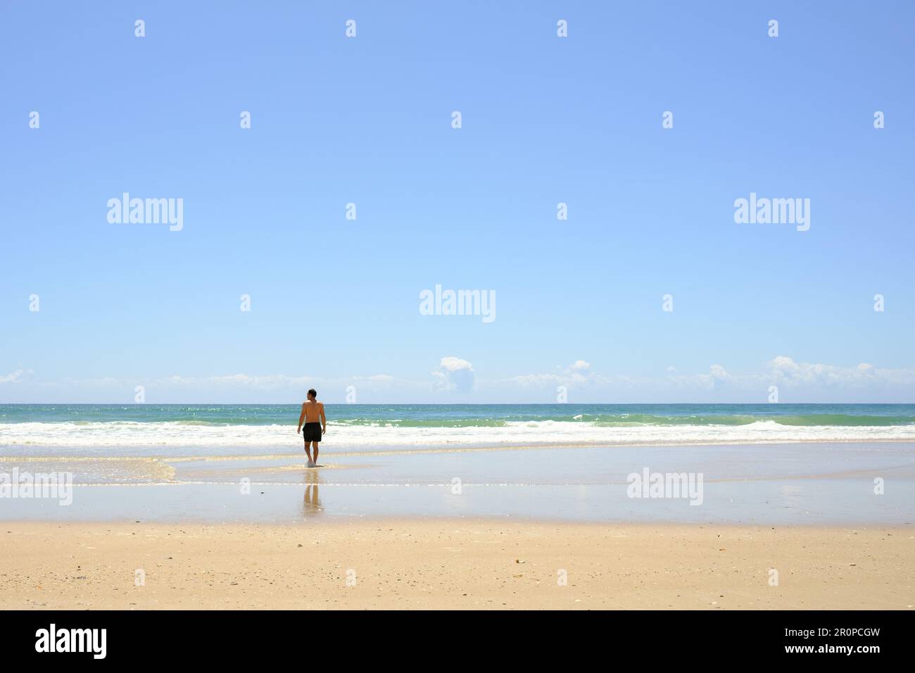 Ein Mann, der über einen Sandstrand spaziert und einen malerischen Ozean überblickt, Noosa North Shore Beach Stockfoto