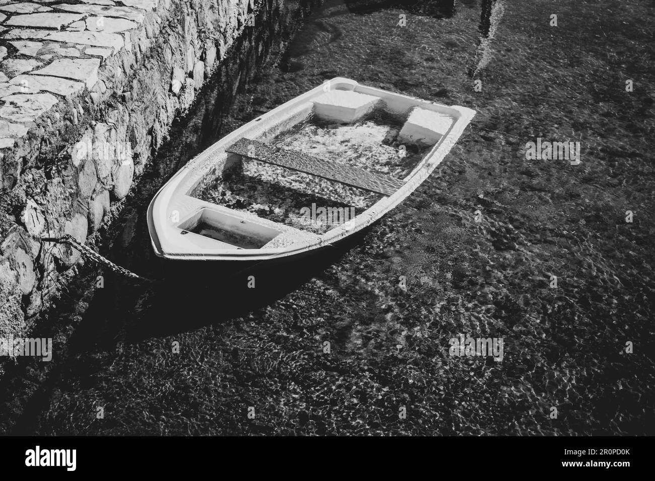 Ein altes Holzboot, das an einem Dock befestigt ist und an einem sonnigen Tag auf dem Wasser schwimmt Stockfoto