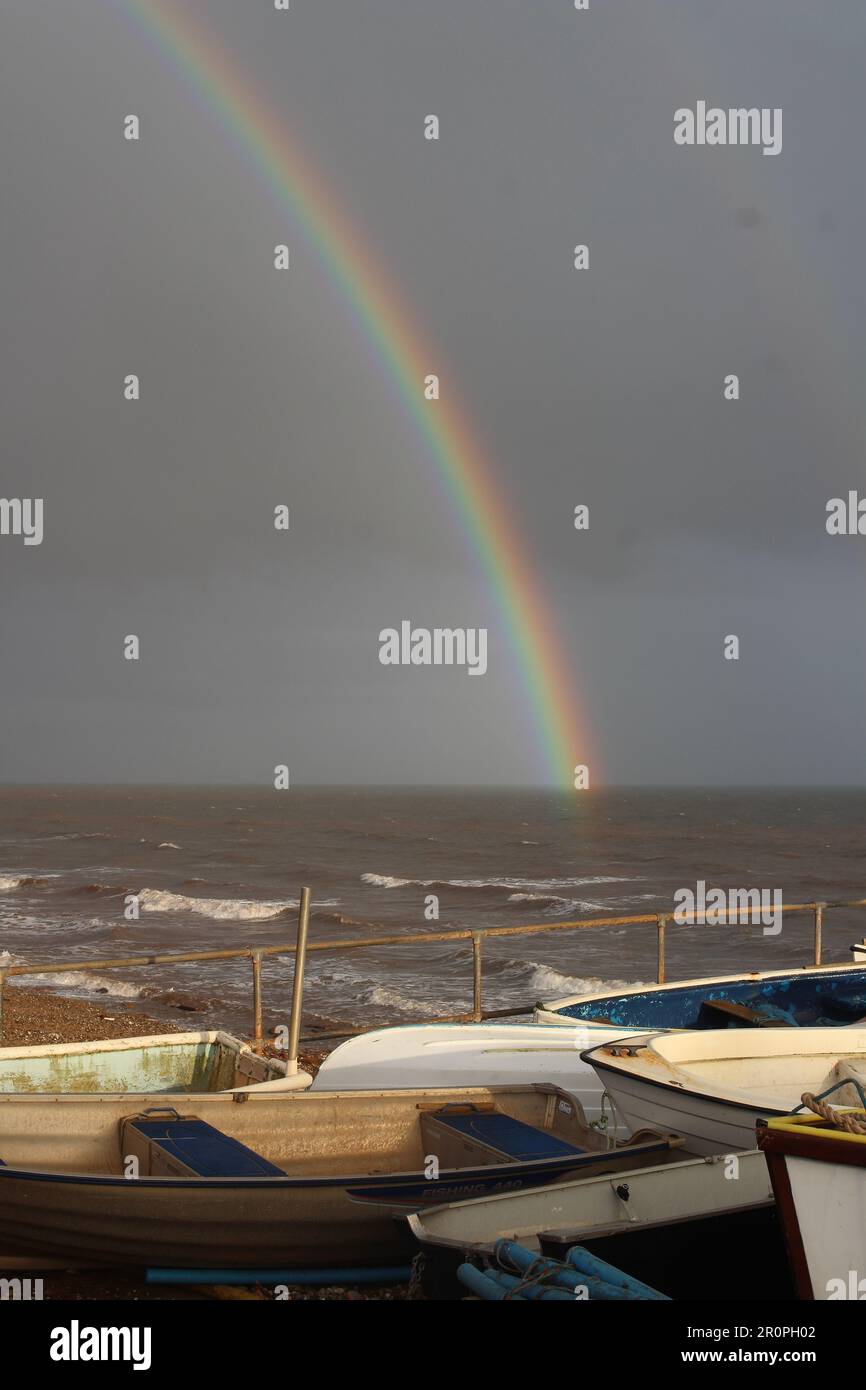 SIDMOUTH, DEVON, Großbritannien - 2. MÄRZ 2017 Regenbogen über dem Meer mit dunklen Wolken und Fischerbooten Stockfoto