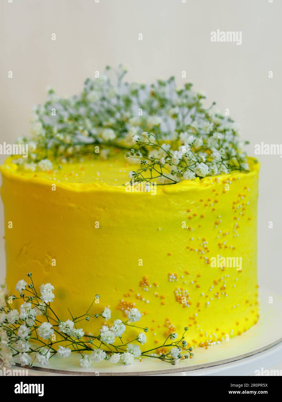 studioaufnahme von gelbem Kuchen mit Frostbecher und weißen Wildblumen auf weißem Hintergrund Stockfoto