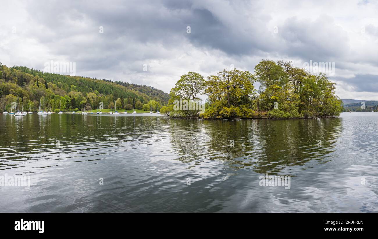 Eine kleine Insel, die nur von Bäumen bewohnt ist, die in einem mehrfarbigen Panorama vor der Mitchell Wyke Ferry Bay in Lake Windermere zu sehen sind. Stockfoto