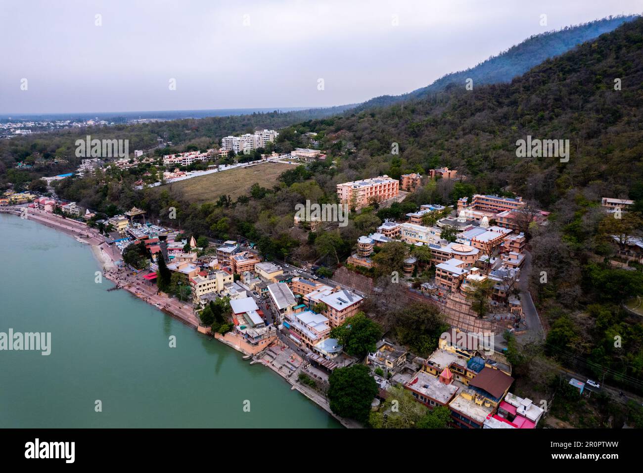 Luftaufnahme von Gebäuden, Wohnungen und Tempeln am Ufer von ganga inmitten dichter Bäume im himalaya-Gebirge in rishikesh haridwar in Stockfoto