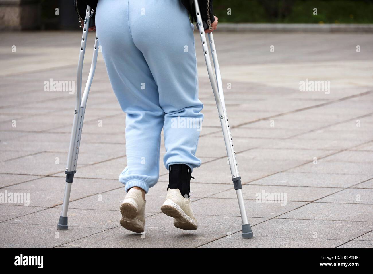 Frau läuft mit Krücken auf einer Straße, weibliche Beine auf dem Bürgersteig. Beinverletzung, Fraktur oder Verstauchung Stockfoto