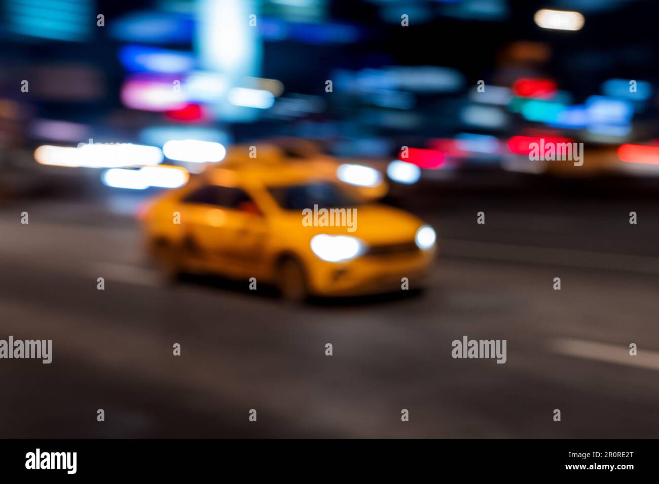 Unscharfer Hintergrund mit gelbem Taxi bewegt sich schnell auf der Stadtstraße zwischen Wolkenkratzern. Unscharfe Beleuchtung von Gebäuden und fahrendem Auto Stockfoto