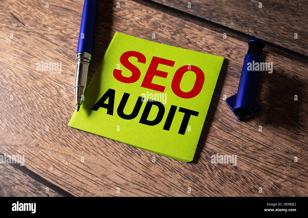 Auf einem hellen Bürotisch befinden sich ein Computer, ein schwarzer Taschenrechner, ein Stift und ein Notizbuch mit dem Text SEO AUDIT. Geschäftskonzept. Stockfoto