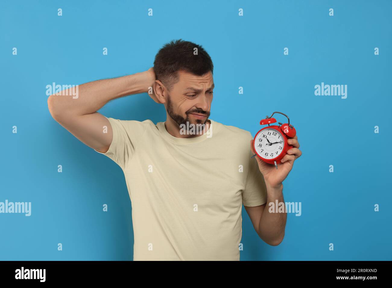 Emotionaler Mann mit Wecker auf hellblauem Hintergrund. Das Konzept der Verspätung Stockfoto