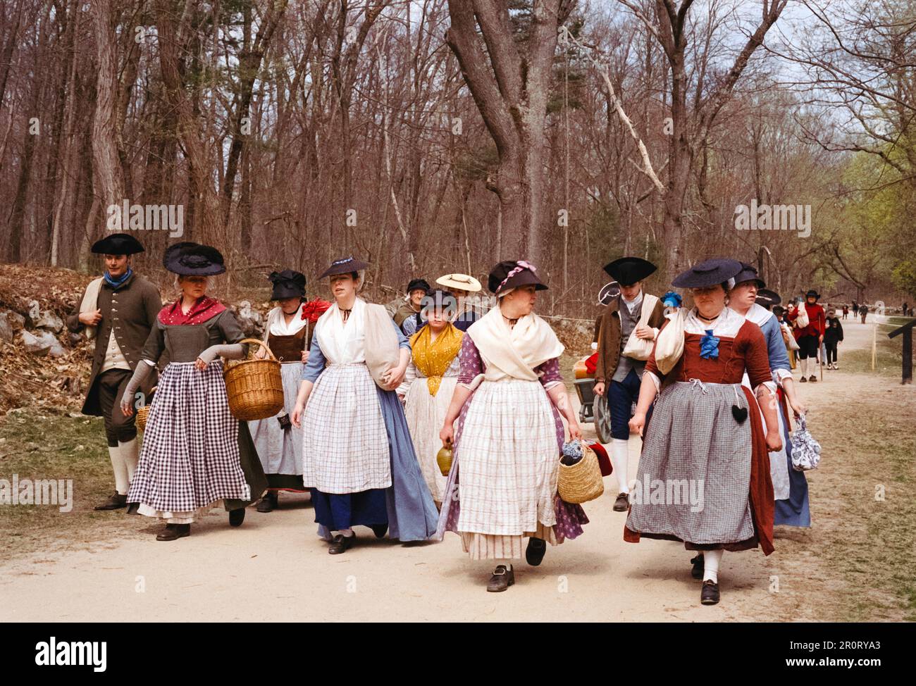 Lexington, Massachusetts, USA - April 2023 - Frauen und Kinder im Kolonialstil spazieren mit all ihren Gegenständen auf der Schlachtstraße in Minutenschnelle Stockfoto