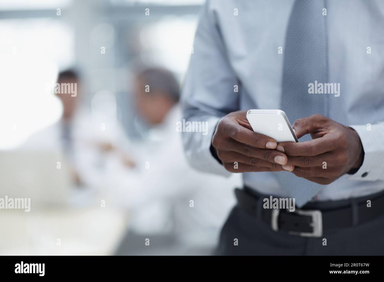 Die Geschäftswelt in greifbarer Nähe. Eine Nahaufnahme eines afrikanischen Geschäftsmanns, der ein Handy hält, mit Kollegen, die im Hintergrund arbeiten. Stockfoto