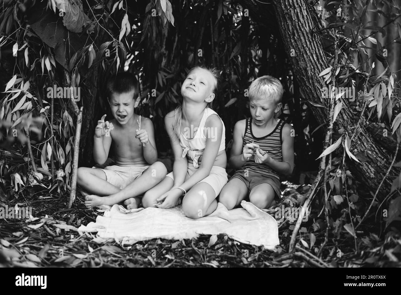 Drei Kinder spielen in einer Hütte, die sie selbst aus Blättern und Zweigen gebaut haben. Schwarzweißfotografie Stockfoto