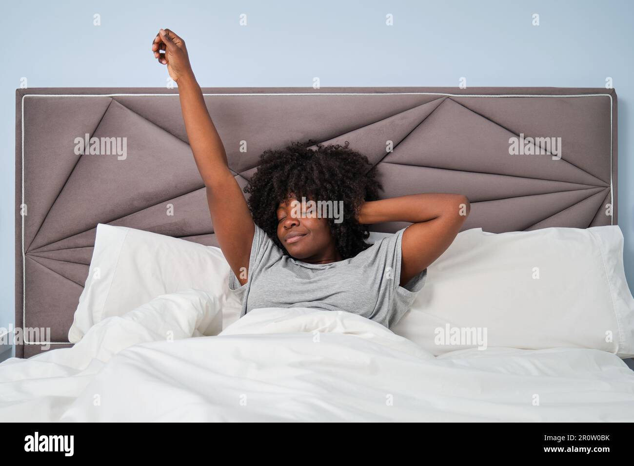 Glückliche afrikanische lächelnde Frau, die sich morgens auf dem Bett ausstreckt. Stockfoto