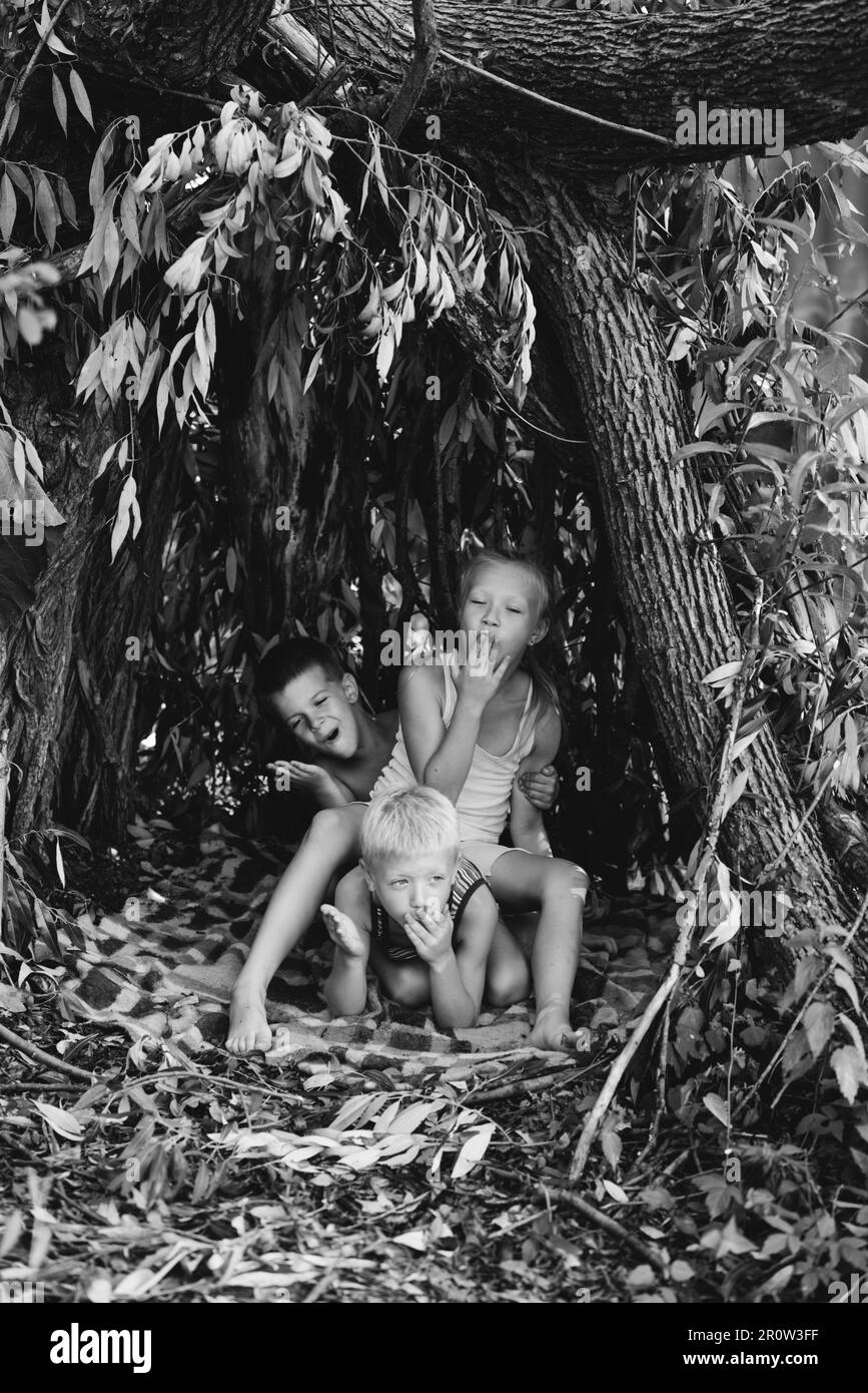 Drei Kinder spielen in einer Hütte, die sie selbst aus Blättern und Zweigen gebaut haben. Schwarzweißfotografie Stockfoto