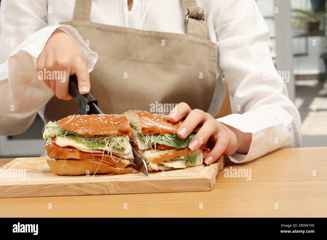 Eine Frau schneidet ein truthahnschinken-, Käse- und Gemüsemilchbrot-Sandwich Stockfoto